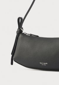 Mustast nahast üleõlakott tekstureeritud viimistlusega, tõmblukuga sulgemine ja reguleeritav rihm. Omab hõbedast riistvara ja reljeefse brändilogoga.