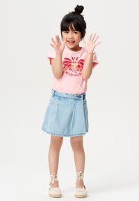 Różowa koszulka z czerwoną tropikalną grafiką, zestawiona z jasnoniebieską dżinsową spódnicą i beżowymi espadrylami z wiązaniami przy kostkach.