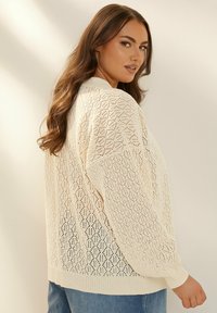 Krämfärgad stickad tröja med diamantmönster, med en avslappnad passform, ribbade manschetter och rundad halsringning. Buren över denim.