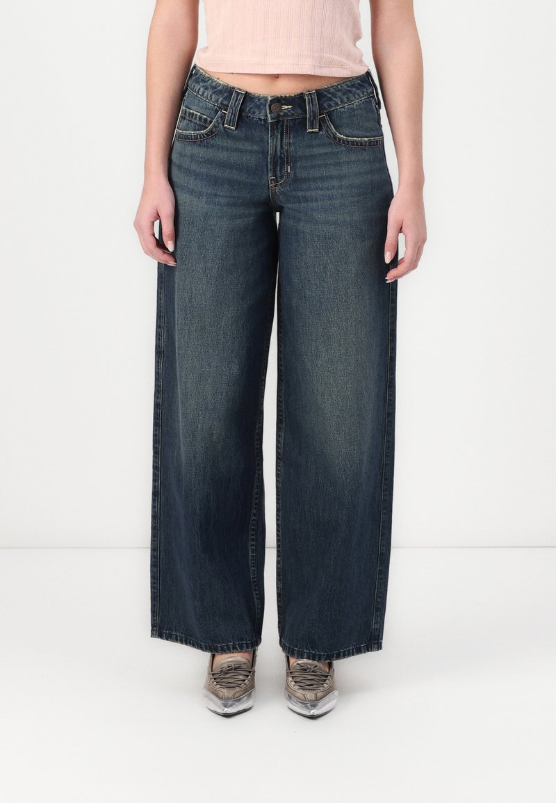 Široke temne jeans hlače z visokim pasom, ki imajo sprednje žepke, kovinsko zapiranje na gumb in kontrastno šivanje. Primerne za vsakodnevno nošenje.