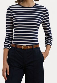 Randig långärmad tröja i marinblått och vitt, med rundad halsringning. Matchas med mörkblå byxor och ett brunt bälte med ett guldfärgat spänne.