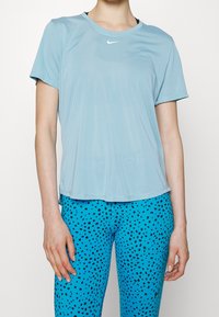 Camiseta atlética de manga corta azul claro con cuello redondo y sutil logo de Nike, combinada con leggins azules texturizados con puntos negros.