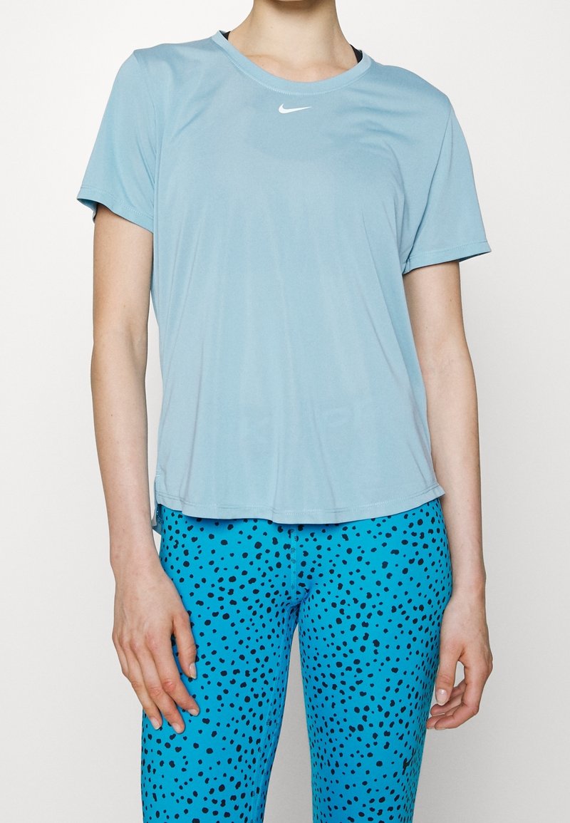 Camiseta atlética de manga corta azul claro con cuello redondo y sutil logo de Nike, combinada con leggins azules texturizados con puntos negros.