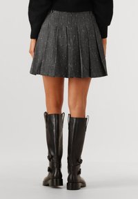 Zwarte plissé rok met zilveren draadaccenten, gemaakt van een gestructureerde stof, gecombineerd met hoge zwarte leren laarzen met gespen.