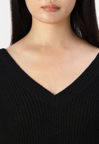 Maglione nero lavorato a maglia con scollo a V, tessuto texturizzato e silhouette aderente, che accentua uno stile casual.