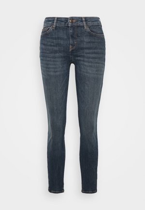 Dark blue denim jeans with a slim fit, featuring a button and zipper fly, five pockets, and slight fading details on the fabric.