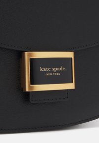 Black leather handbag featuring a gold-tone hardware plaque with "kate spade NEW YORK" branding and a textured finish.