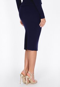 Navy Midi-Rock aus Strick mit einem leichten Schlitz, kombiniert mit metallisch goldenen High-Heeled Sandalen. Strukturiertes Material mit taillierter Passform.
