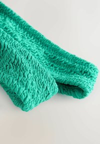 Kihiline, kortsuline akvamarinfabric, millel on pehme, kootud välimus ja rippuv disain. Rullub mugsalt kokku, nähtavate õmblusdetailidega.