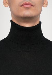 Svart ribbad polotröja med hög hals och snug passform. Tillverkad av ett mjukt, texturerat stickat tyg.