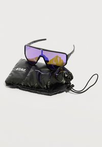 Μαύρα αθλητικά γυαλιά ηλίου με μοβ φακούς που ακουμπούν σε μια μαύρη θήκη με κορδόνι και λευκή εμπορική σήμανση σε απλό φόντο.