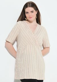 Kurzärmlige, wickelartige Bluse in Creme mit vertikalen, mehrfarbigen Streifen. Weicher Stoff mit strukturierter Oberfläche und V-Ausschnitt.