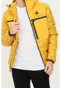 Doudoune jaune avec capuche, dotée d'une poche poitrine zippée et de poignets élastiques. Confectionnée en matière légère et matelassée.