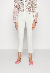 Pantaloni bianchi a vita alta con taglio sartoriale e cuciture frontali, abbinati a scarpe slip-on in velluto rosa, su uno sfondo neutro.