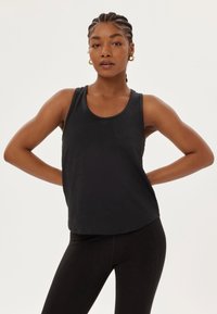 Débardeur noir sans manches avec un col arrondi, fabriqué à partir d'un matériau lisse; associé à des leggings noirs au design ajusté.