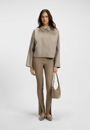 Fitted beige wool cropped jacket, high collar, paired with beige leather pants featuring side slits. Model holds a matching handbag.