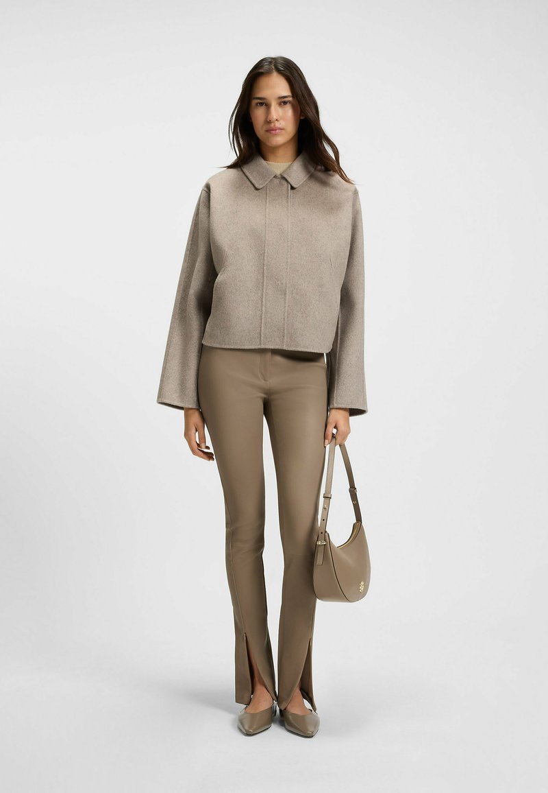 Fitted beige wool cropped jacket, high collar, paired with beige leather pants featuring side slits. Model holds a matching handbag.
