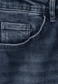Mörkblå denimtyg av jeans, med en framficka med sömnadsdetaljer, jämn textur och subtila bleknade områden.