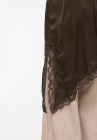 Tissu en satin brun foncé avec bordure en dentelle florale sur un pantalon en lin beige, sur fond blanc.