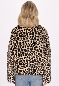 Geacă din blană ecologică cu model de leopard, cu o textură moale, umeri rotunzi și o croială lejeră, asortată cu blugi din denim deschis.