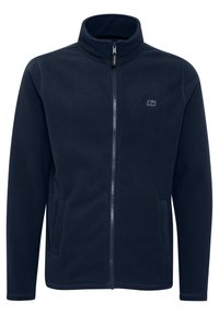 Chaqueta de forro polar azul marino con cuello alto, cremallera completa, bolsillos laterales y un logo sutil en el pecho. Textura suave y corte recto.