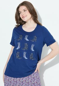 Námořnická modrá tričko s krátkým rukávem, které zobrazuje grafiku různých kovbojských bot v kontrastních barvách. Měkká tkanina s kulatým výstřihem.