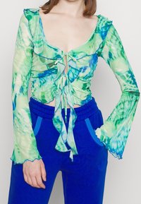Green and blue tie-dye long-sleeve top with ruffled neckline and cuffs, featuring drawstring front and ruched design. Paired with blue sweatpants.