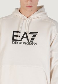 Lichtbeige hoodie gemaakt van zacht stof; voorzien van een geborduurd zwart logo "EA7 EMPORIO ARMANI" op de voorkant; inclusief een capuchon met trekkoord.