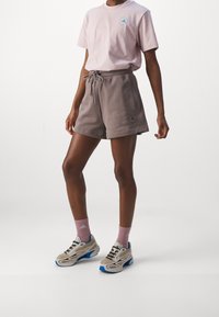 Camiseta de color rosa claro con logotipo, pantalones cortos grises con cordón y emblema, calcetines rosas y zapatillas grises con acentos azules. Conjunto de ropa activa casual.