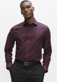 Bourgognefarvet skjorte med knapper, et subtelt mønster, lange ærmer og krave, kombineret med sorte bukser og sort bælte.