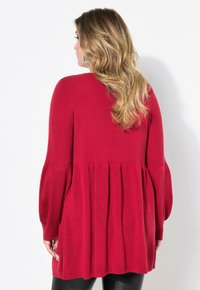 Roter gestrickter Pullover mit einem gefalteten Design, langen Ärmeln und einem lockeren Schnitt. Ausgestattet mit einem strukturierten Stoff und einer einfarbigen Optik ohne Muster.