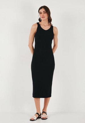 Black ribbed midi dress with a scoop neckline and fitted shape, paired with black and white strappy sandals. Smooth texture, versatile design.