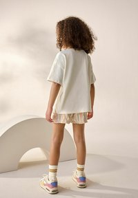 T-shirt en coton blanc à manches courtes, associé à un short texturé multicolore. Le mannequin porte des baskets pastel et des chaussettes rayées.