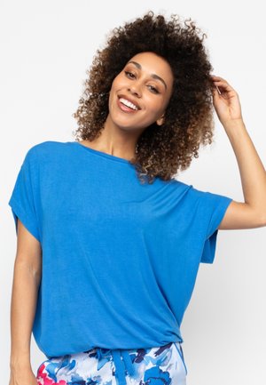 Blauses Kurzarmtop aus leichtem Stoff, mit einem lässigen Schnitt und rundem Halsausschnitt. Kombiniert mit gemusterten Shorts.