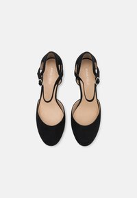 Chaussures à talons en daim noir avec un bout arrondi, un design découpé et une sangle ajustable avec une boucle en argent. Semelle intérieure beige douce visible.