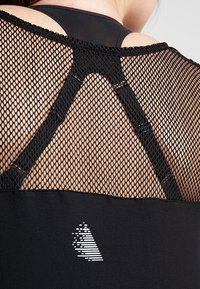 Zwarte sportieve tanktop met een mesh achterkant, een gladde onderzijde en een grafische accent aan de zijkant. Gestikte details zijn zichtbaar.