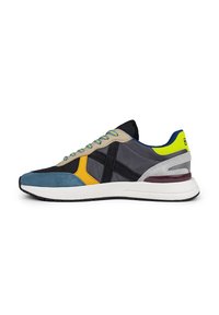 Zapatillas para hombres que presentan una combinación de tejidos en azul, gris, amarillo y negro; diseño elegante con una entresuela blanca y acentos texturizados.