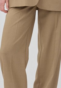 Pantalons beige sur mesure avec une texture lisse, un design à jambes larges et des plis nets à l'avant et à l'arrière, présentant une coupe classique.