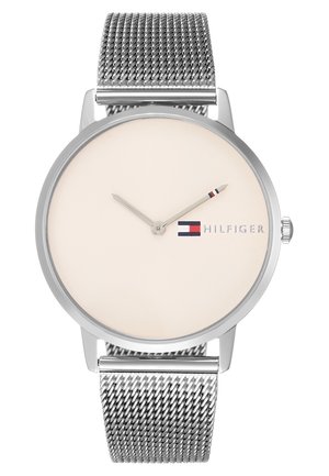 Montre-bracelet argentée minimaliste avec bracelet en maille, cadran beige, deux aiguilles et logo Tommy Hilfiger rouge-blanc-bleu près de la position 3 heures.