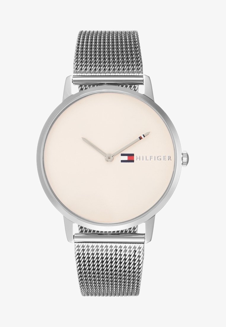 Montre-bracelet argentée minimaliste avec bracelet en maille, cadran beige, deux aiguilles et logo Tommy Hilfiger rouge-blanc-bleu près de la position 3 heures.
