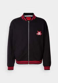 Black bomber jacket with red ribbed collar and cuffs. Features a front zipper and embroidered logo detail at chest. Cotton blend material.