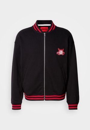 Black bomber jacket with red ribbed collar and cuffs. Features a front zipper and embroidered logo detail at chest. Cotton blend material.