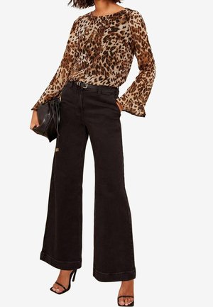Femme portant un chemisier manches longues à imprimé léopard, un pantalon noir taille haute à jambes larges, ceinture noire, tenant un sac à main noir et des sandales noires à talons.