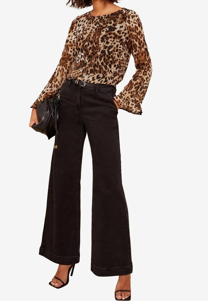 Femme portant un chemisier manches longues à imprimé léopard, un pantalon noir taille haute à jambes larges, ceinture noire, tenant un sac à main noir et des sandales noires à talons.