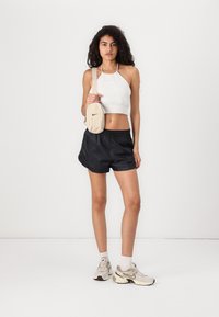 Gray halter crop top, black athletic shorts, and light gray sneakers with dark accents. Beige crossbody bag with a black logo detail.
