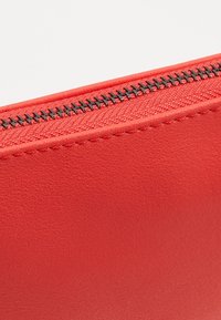 Červená taštička na zip vyrobená z texturované umělé kůže. Obsahuje kontrastní černý zip a hladké okraje. Kompaktní a obdélníkový design.