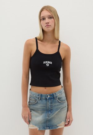 Top corto negro con canalé y texto blanco "PALM BEACH", combinado con una falda mini de mezclilla desgastada que presenta un dobladillo deshilachado y bolsillos frontales.
