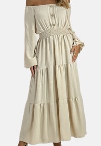 Off-shoulder, crèmekleurige jurk met een gesmockte taille, lange mouwen, drie knopen en een geplooide, gerimpelde zoom. Zachte textuur.