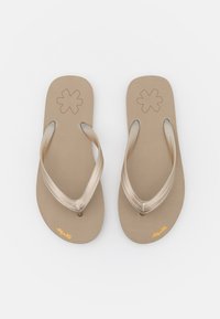 Flip-flops with a smooth beige sole, metallic gold straps featuring a textured design, and a flower emblem on each footbed.