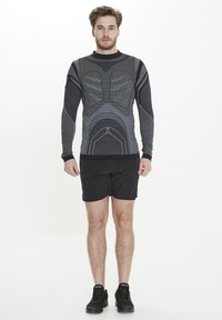 Svart atletisk långärmad topp med texturerade mönster och grå detaljer, matchad med svarta shorts och mörka sportskor.